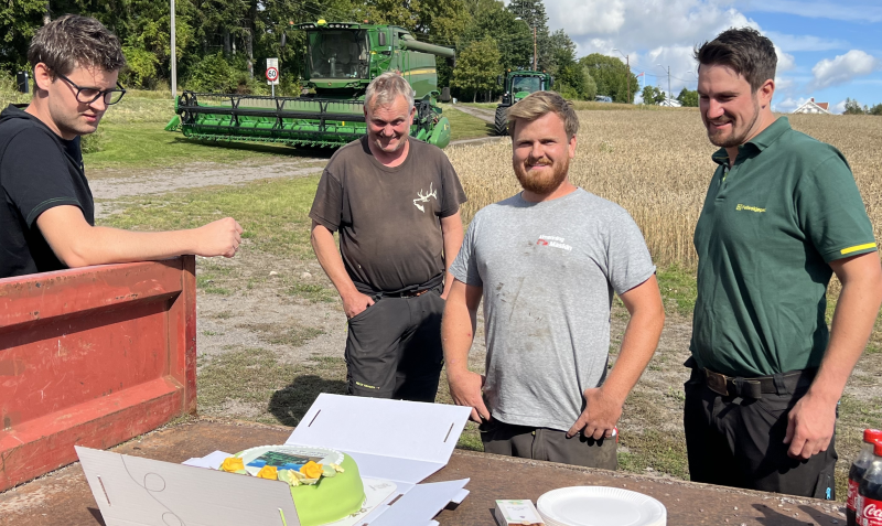 Fire karer spiser kake ved tilhenger med skurtresker i bakgrunnen.