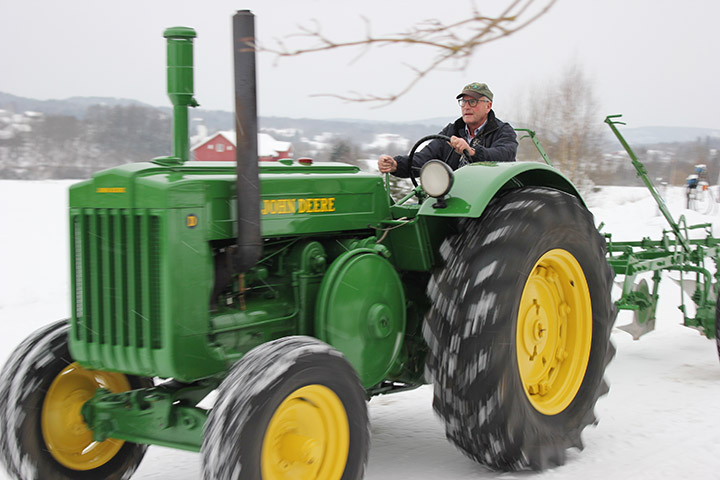 Mann kjører veterantraktor i vinterlandskap