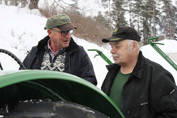 To eldre menn i samtale bak traktor