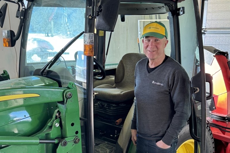 Mann med caps foran John Deere traktor