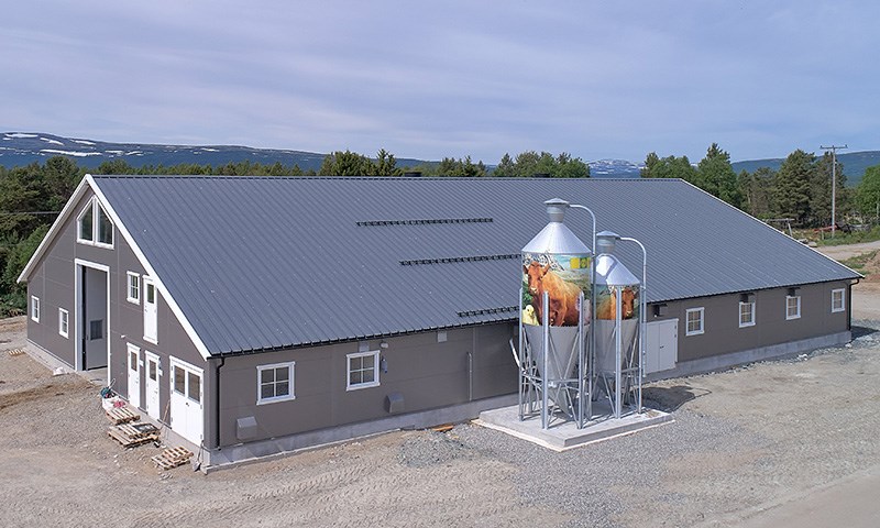 Ny grå driftsbygning med stor port og to kraftfôrsiloer på langveggen.