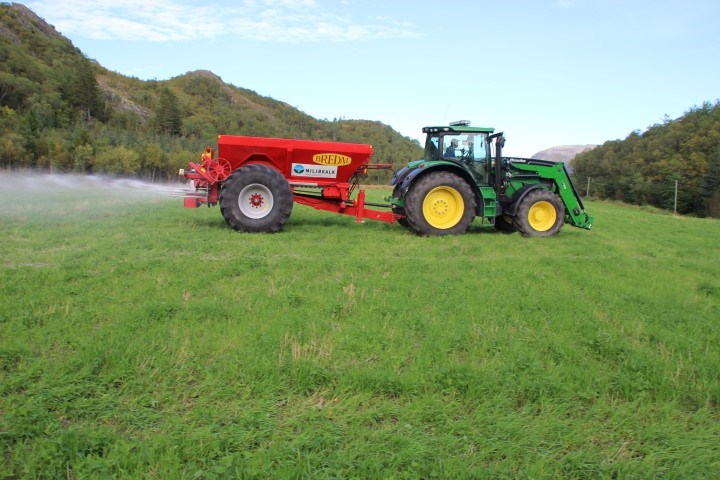 Traktor med kalkvogn på jordet som sprer kalk. Foto.