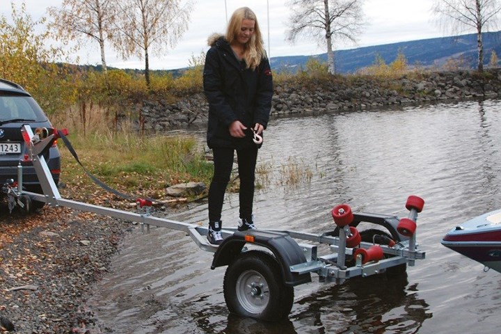 Kvinne står mellom en bil og en båthenger, båten ligger på vannet